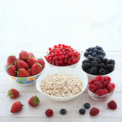 Berries, strawberries, raspberries, currants, blackberries, blueberries, nuts, milk and muesli  ingredients for healthy breakfast  on white wooden table.