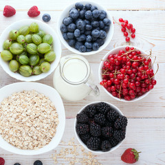 Berries, strawberries, raspberries, currants, blackberries, blueberries, nuts, milk and muesli  ingredients for healthy breakfast  on white wooden table.