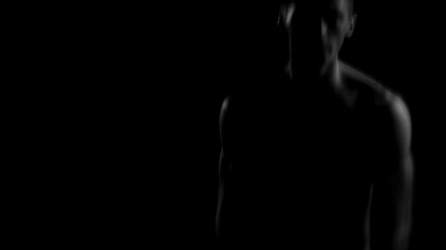sexy naked guy with a nice athletic body dancing on a black background in the dark