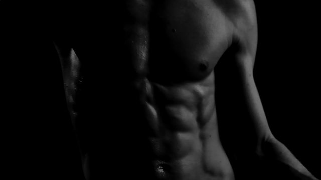 Perfect naked male torso muscles moving in the darkness close up