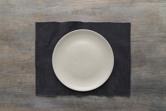An off-white plate on a black placemat on a wooden table
