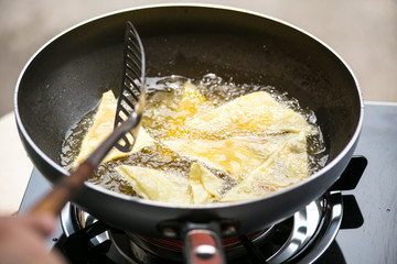 Dough sheet deep frying in very hot oil.