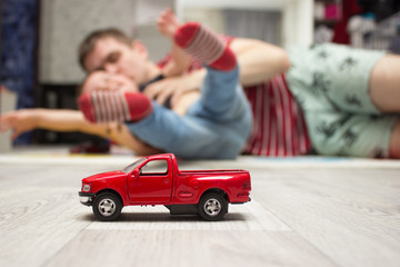 Red toy car, father and son playing at background