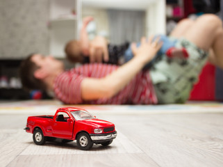 Red toy car, father and son playing at background