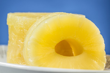 Canned pineapple slices, preserved at its own juice, on oval dish and blue background