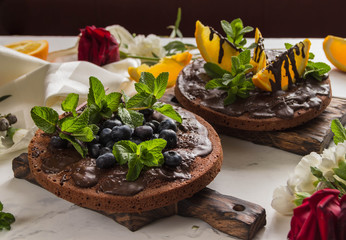 Chocolate cakes with chocolate frosting and orange, and blueberries,mint.