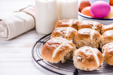 Hot cross bun on tray with Easter vibrant eggs and milk.
