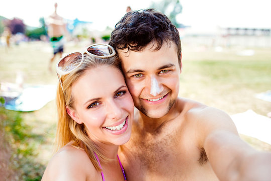 Young couple sunbathing, taking selfie. Sunscreen on the nose.
