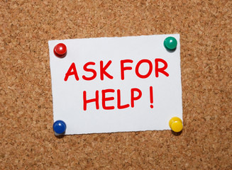 The phrase Ask For Help typed on a white piece of note paper and pinned to a cork notice board