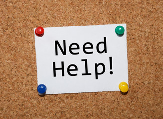 The phrase Need Help!  typed on a white piece of note paper and pinned to a cork notice board