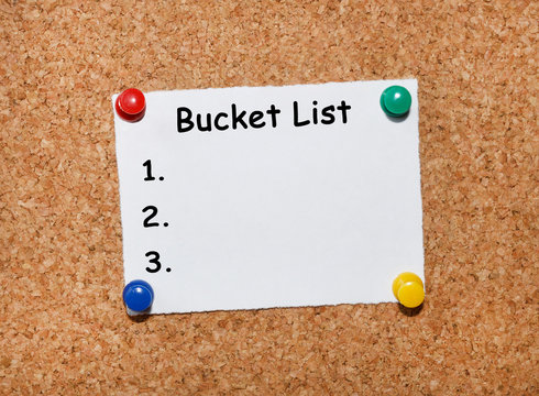 The phrase Bucket list  typed on a white piece of note paper and pinned to a cork notice board