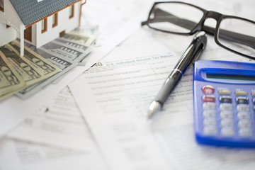 Miniature house with money on tax papers