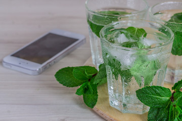glass of cold water with fresh mint leaves and ice cubes on wood