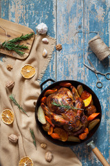 Roasted chicken stuffed with various vegetables and spices in cast iron skillet on vintage wooden table background. Top view, rustic style.