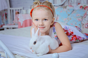 little 8 years girl in a pink suit sitting on a bed among pillows with white rabbit © biotin