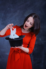 Teacher of of Magic. Young beautiful girl in a red dress holds a black illusionist hat with a white...