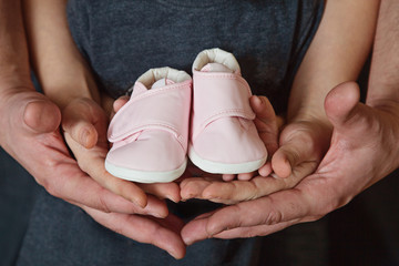 Future parents holding a pair of little shoes in their hands. Hands of parents and kid holding a pair of little shoes. Waiting for a new family member. Selective focus