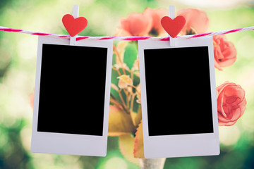 2 Blank instant photo and red clippaper heart hanging on the clothesline with pink rose flower background. vintage tone.Designer concept.