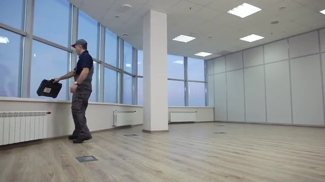 Service Employee Checks the Order at the Office/Service employee enters into an empty office and pulls out a tool for assembling furniture. Spacious office with large, bright windows. Dolly