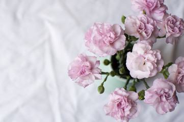 High angle view of pink carnations in a green vase on a white tablecloth