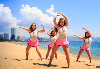 cheerleaders in dance pose hands over head on beach against sea