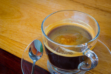 Black expresso coffee in small glass cup on wooden table with te
