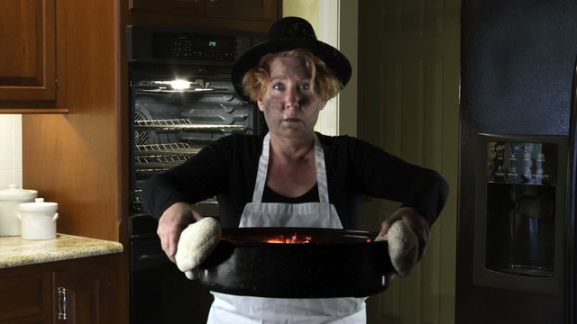 Woman wearing apron with Pilgrim Hat holding buring roasting pan.
