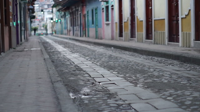 Low angle panning shot of a deserted cobblestone and flagstone road in an historic city district with traffic and an anonymous person far off in the background.