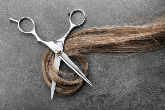 Hairdresser's scissors with strand of brown hair on grey background