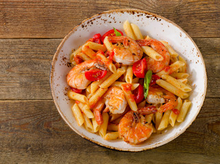 Penne pasta with shrimp and tomatoes  on rustic wooden table.
