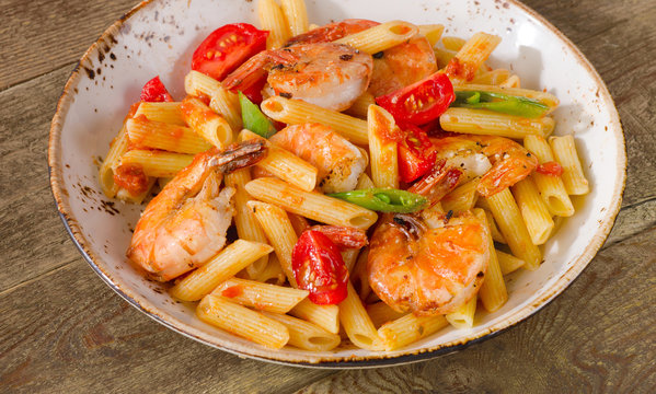 Penne pasta with shrimp and tomatoes  on a rustic wooden table.