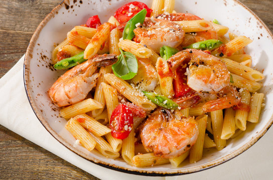Penne pasta with shrimp, tomatoes and herbs on wooden table.