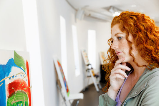 Young caucasian woman standing in art gallery front of  paintings