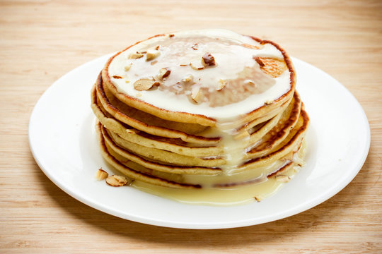 Stack of pancakes with condensed milk and nuts on a white plate