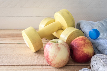 Fitness concept with bottle of water and apple,dumbbells on wood