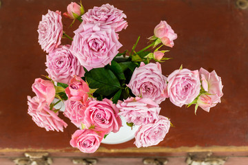 Pink flowers in jug on old brown vintage suitcase. Roses in jug. Pink roses. Shabby chic. Rustic concept.