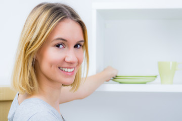 lächelnde hausfrau räumt geschirr ein