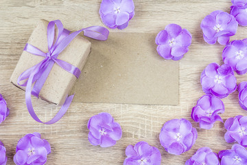 Gift box, purple flowers and blank paper card on wooden backgrou