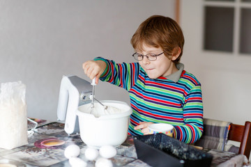 Funny blond kid boy baking cake indoors