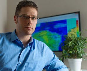 Handsome male meteorologist in glasses on his workplace.