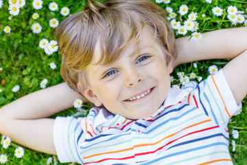 Happy kid boy laying on green grass in summer