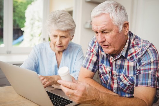 Senior couple holding a pill bottle while operating laptop - Powered by Adobe
