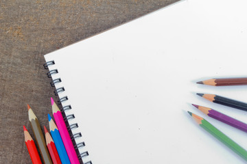 Blank notepad and colorful pencils on the wooden table. View from above