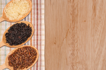 Red, white, and black rice in a wooden spoon on a wooden table