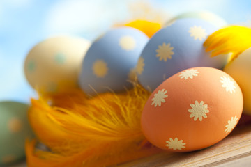 Painted Easter eggs and yellow feathers on sky background