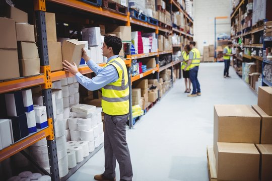 Smiling warehouse worker taking package in the shelf