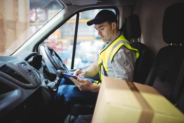 Delivery driver using tablet in van with parcels on seat - Powered by Adobe
