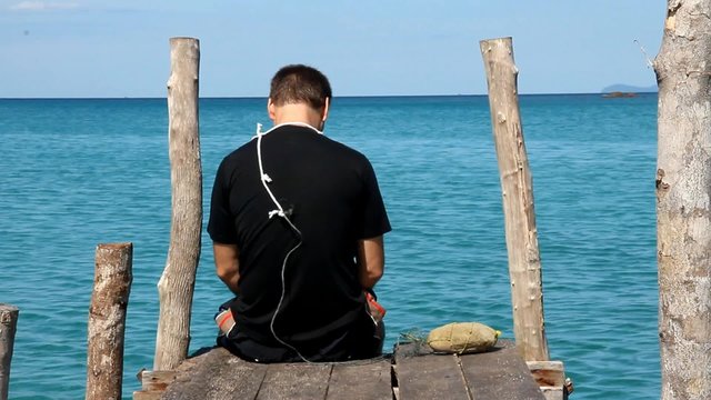 A man sits on a pier over the sea with a noose around his neck