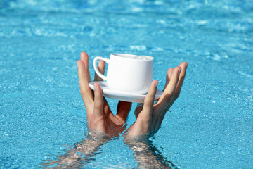 two hands saving a cup and saucer containing some valuable liquid as a symbol of addiction, great value