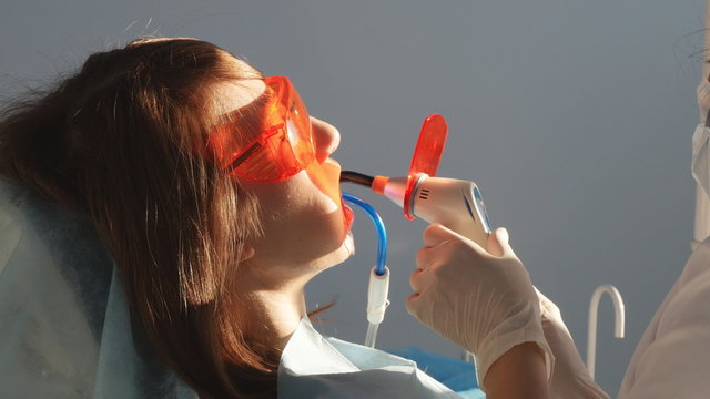 Dentist working with dental polymerization lamp in oral cavity.